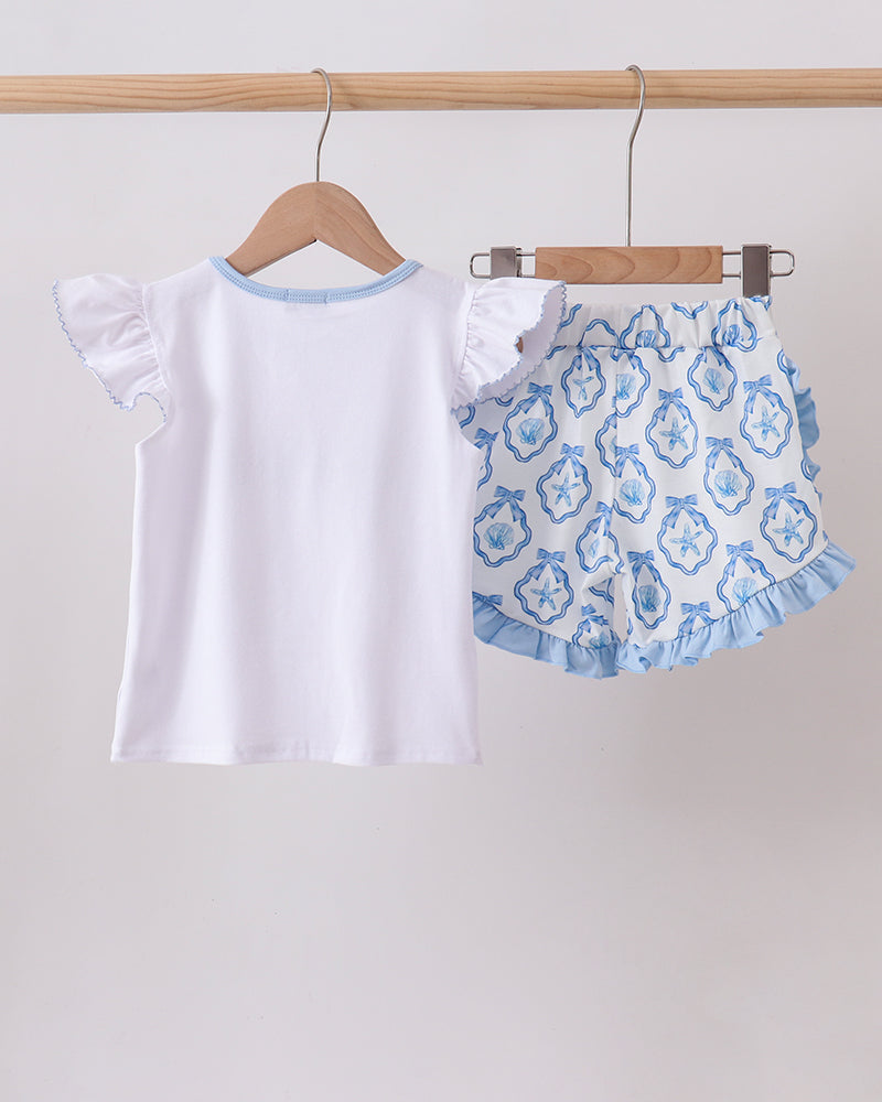 White top with blue trim and patterned shorts on hangers against a white background