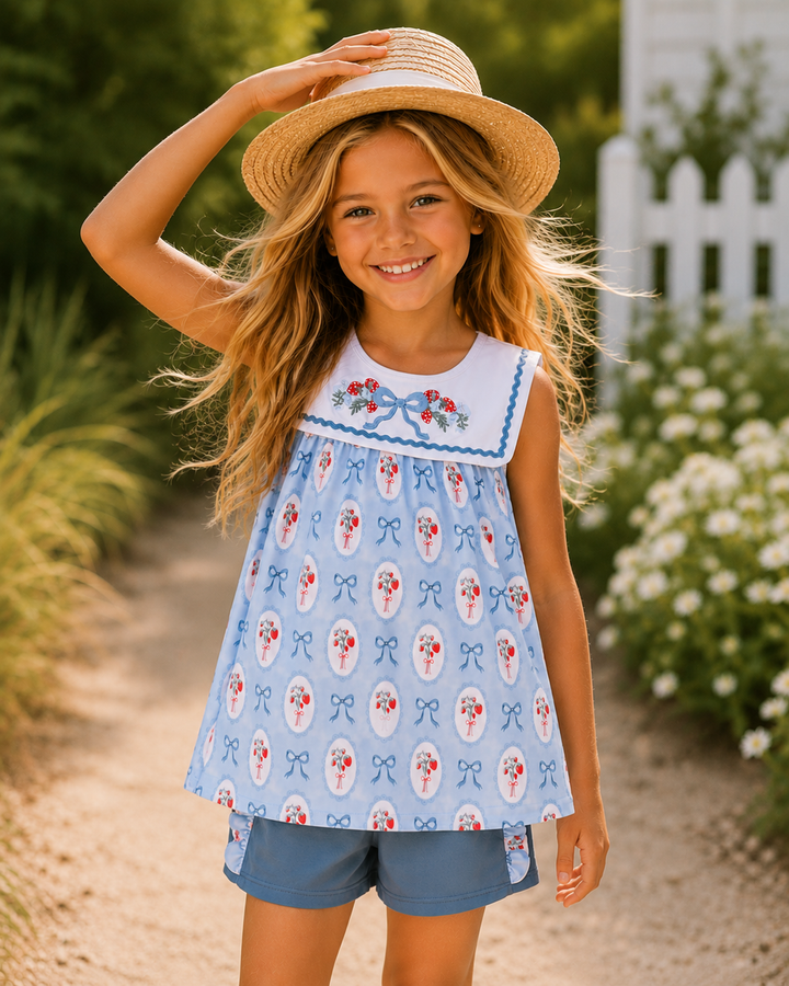 Young girl wearing a light blue dress with floral patterns and a straw hat, standing outdoors.