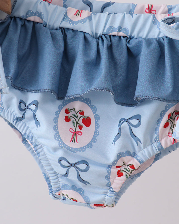 Swim bottoms with blue ruffle and floral pattern on a light gray background
