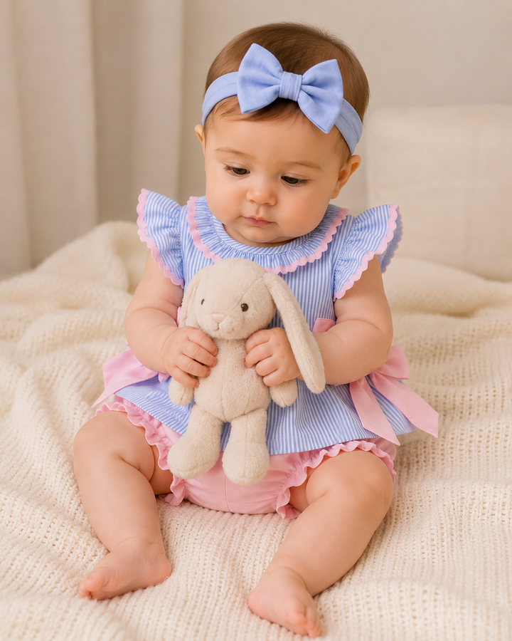Baby girl sitting on a blanket holding a stuffed bunny