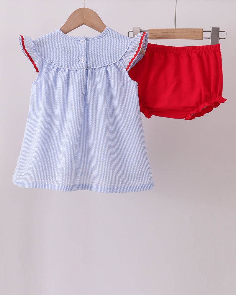 Baby dress with red trim and matching bloomers on a wooden hanger against a light background