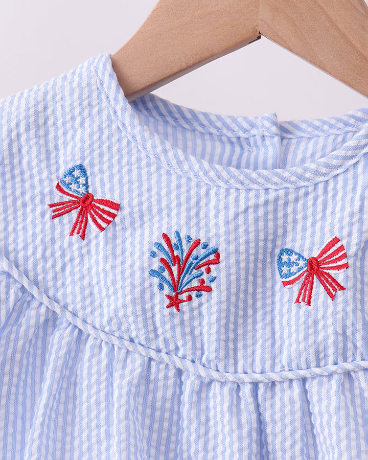 Blue and white striped dress with red, white, and blue embroidered designs on a hanger.