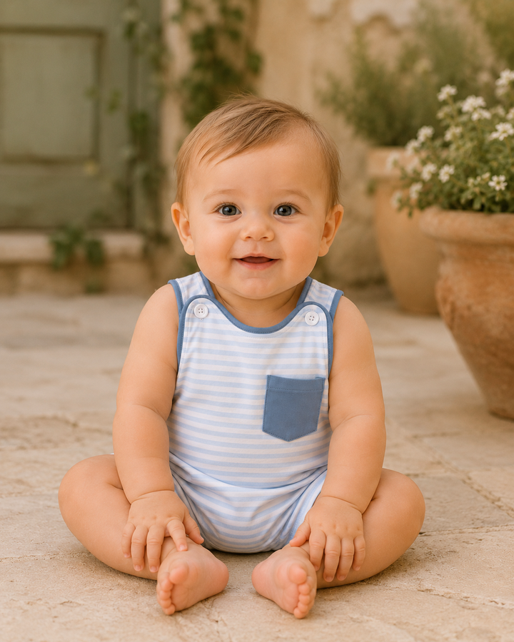 Baby sitting on a stone surface wearing a blue and white striped romper.