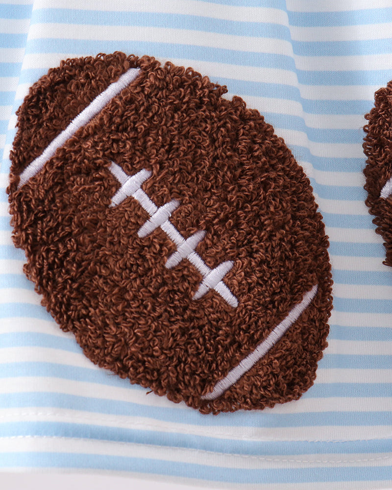 A close-up of a brown football-shaped textured rug with white laces, placed on a light blue and white striped fabric surface.