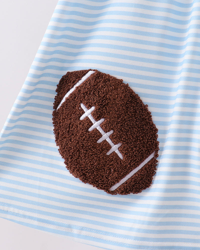 A close-up of a light blue and white striped fabric item featuring a brown football-shaped applique with white laces, photographed on a clean white background.