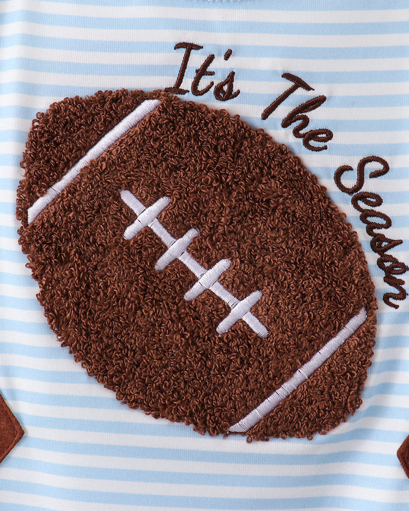 Close-up of a baby shirt with light blue and white horizontal stripes, featuring a large brown textured football applique with white laces and the words &