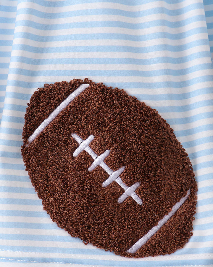 A close-up of a baby blanket featuring a brown textured football applique with white laces on a light blue and white striped fabric background.