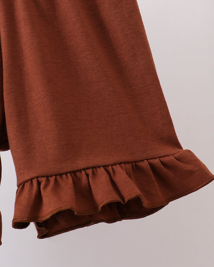 Close-up of a rust brown garment with a ruffled hem, showing the fabric texture and color against a plain light background.