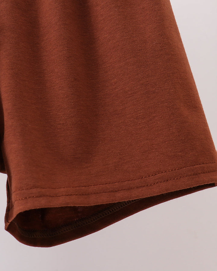 Close-up of a rust-brown short-sleeve t-shirt showing the hem and stitching against a light gray background.