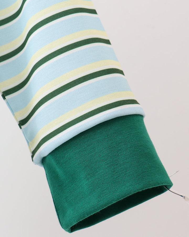 Close-up of a striped long-sleeve garment sleeve with light blue, cream, and dark green horizontal stripes, folded back to show a solid dark green cuff, on a light gray background.