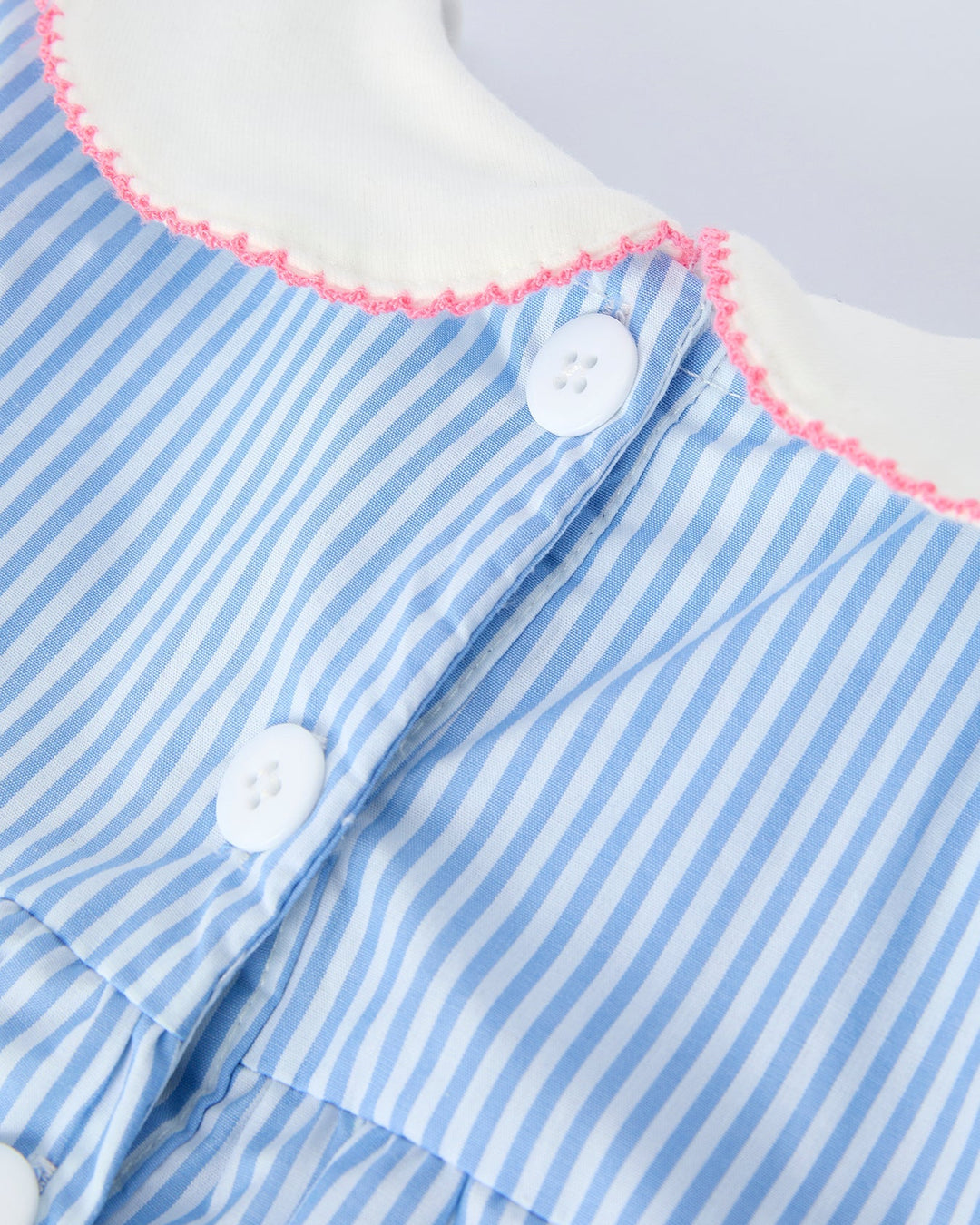 Close-up of a blue and white striped dress with pink trim and white buttons.