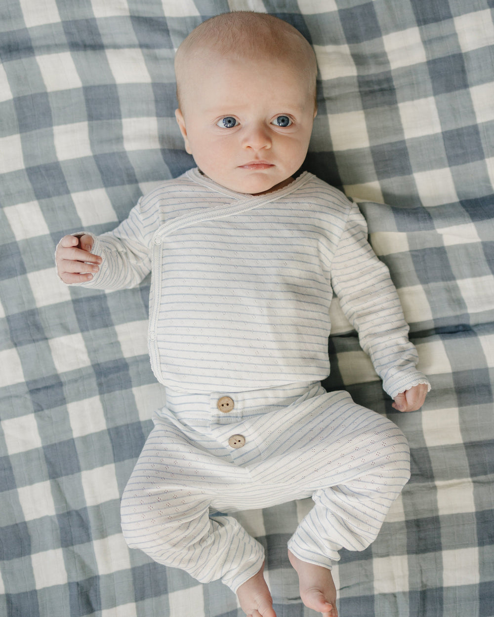 Baby in a striped outfit lying on a checkered blanket