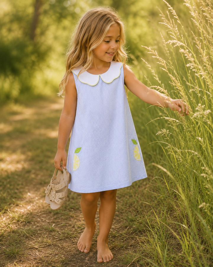 Young girl in a light blue dress with lemon designs standing in tall grass.