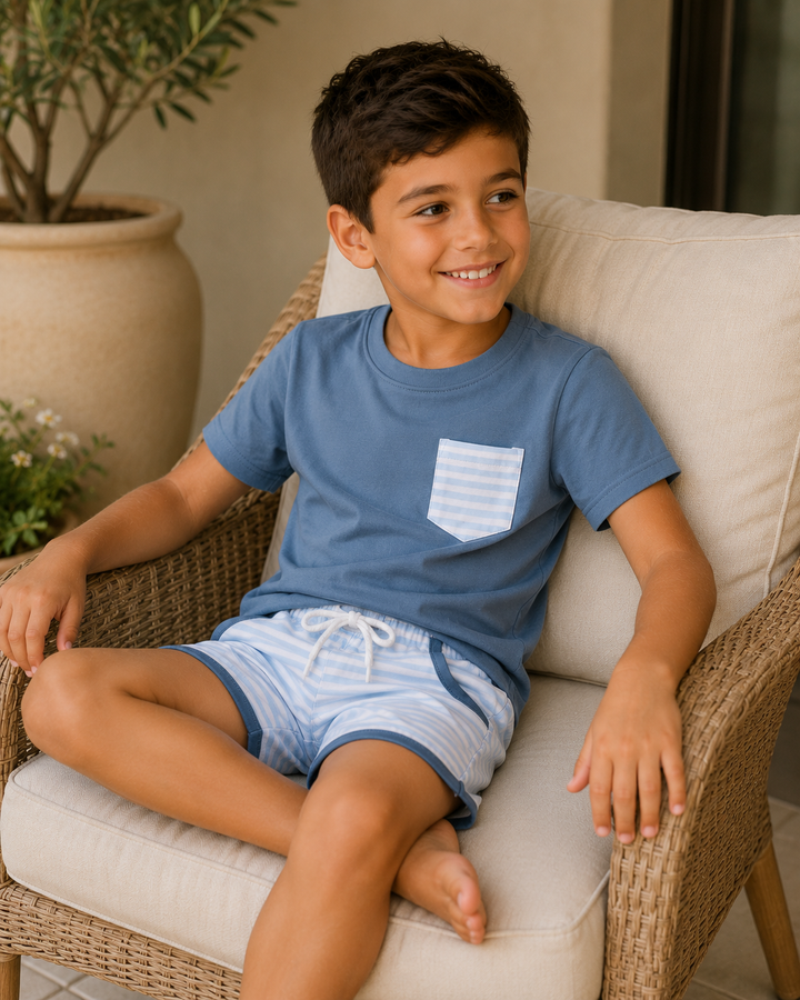Young boy sitting on a chair wearing a blue shirt and light blue shorts, smiling.