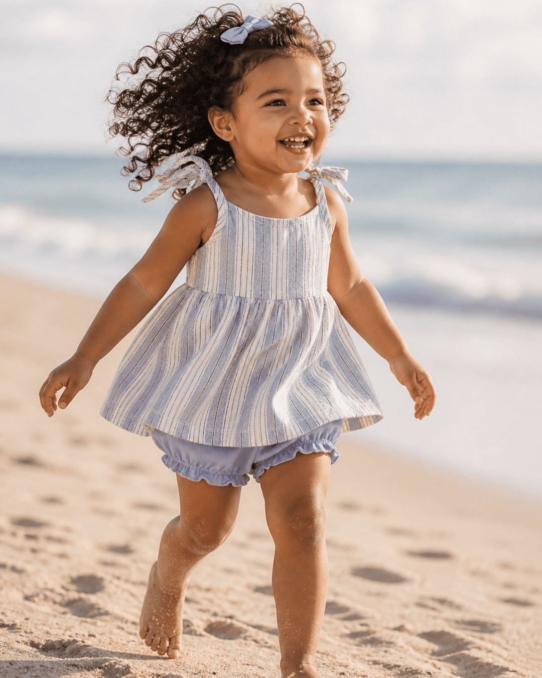 Child in a striped dress running on a sandy beach with ocean in the background