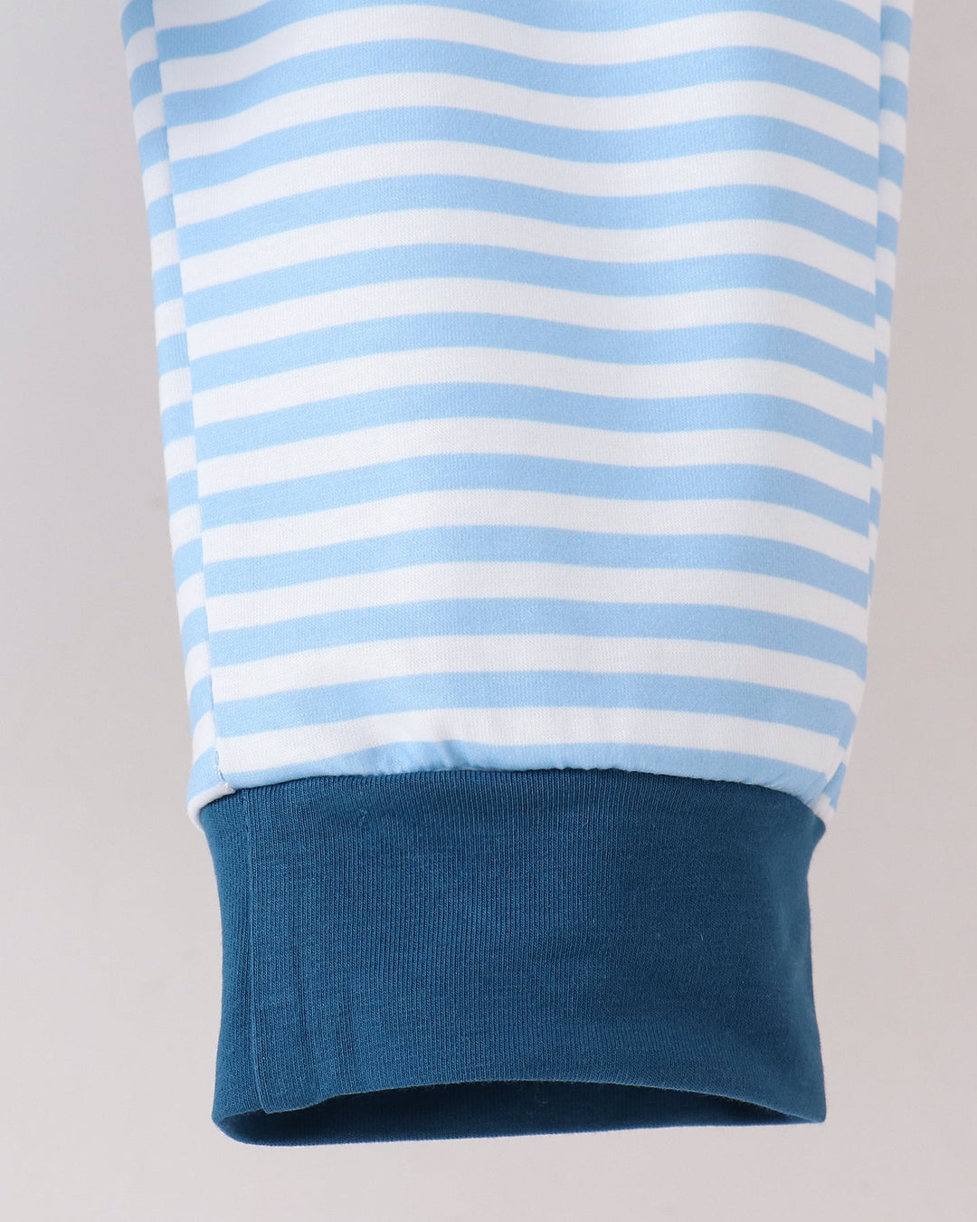 Close-up of a light blue and white striped sleeve with a solid dark blue ribbed cuff, shown against a light gray background.