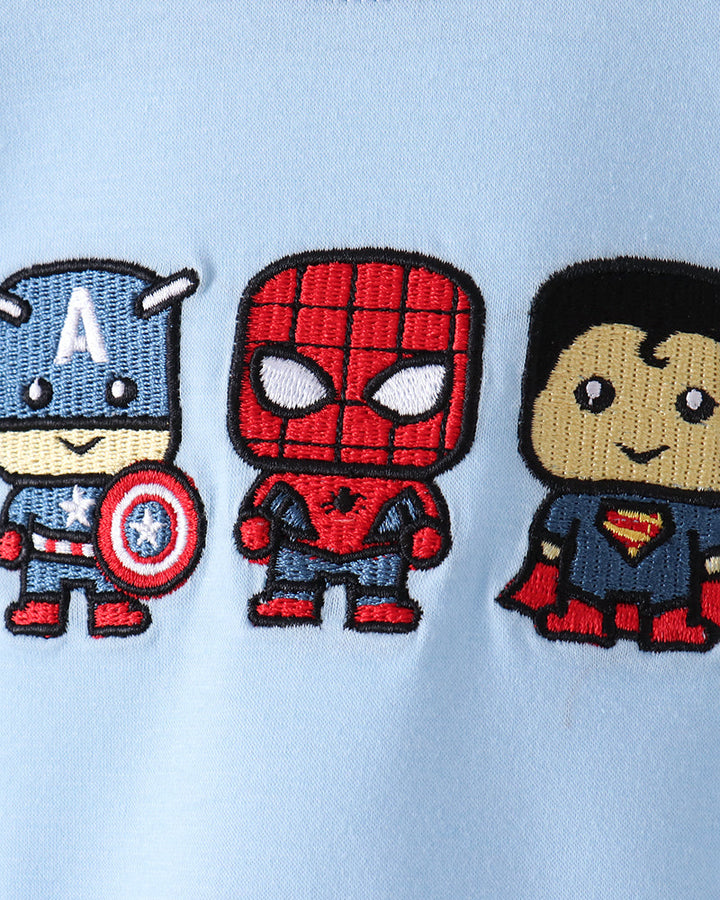 Close-up of a light blue garment featuring three embroidered cartoon superheroes: Captain America, Spider-Man, and Superman, stitched onto the chest.