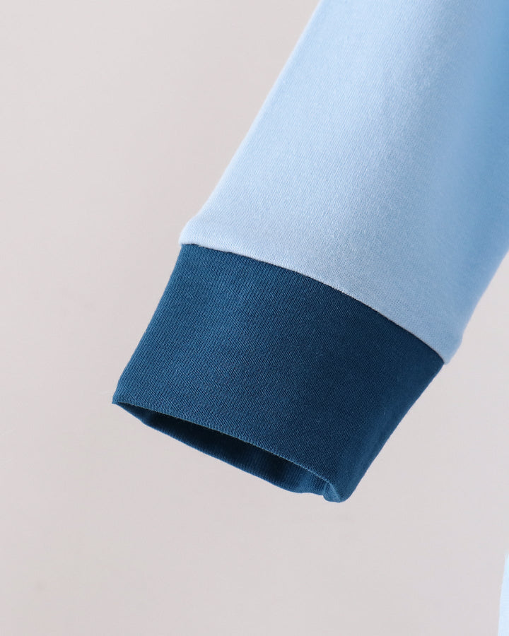 Close-up of a light blue sleeve with a contrasting dark blue ribbed cuff, shown against a plain light background.