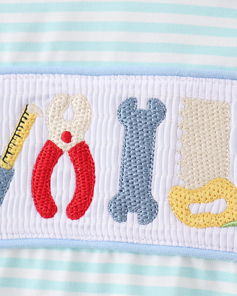 Close-up of tool appliques on white smocked panel atop blue striped romper
