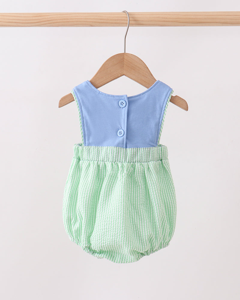 Baby romper with blue top and green checkered bottom on a wooden hanger against a white background