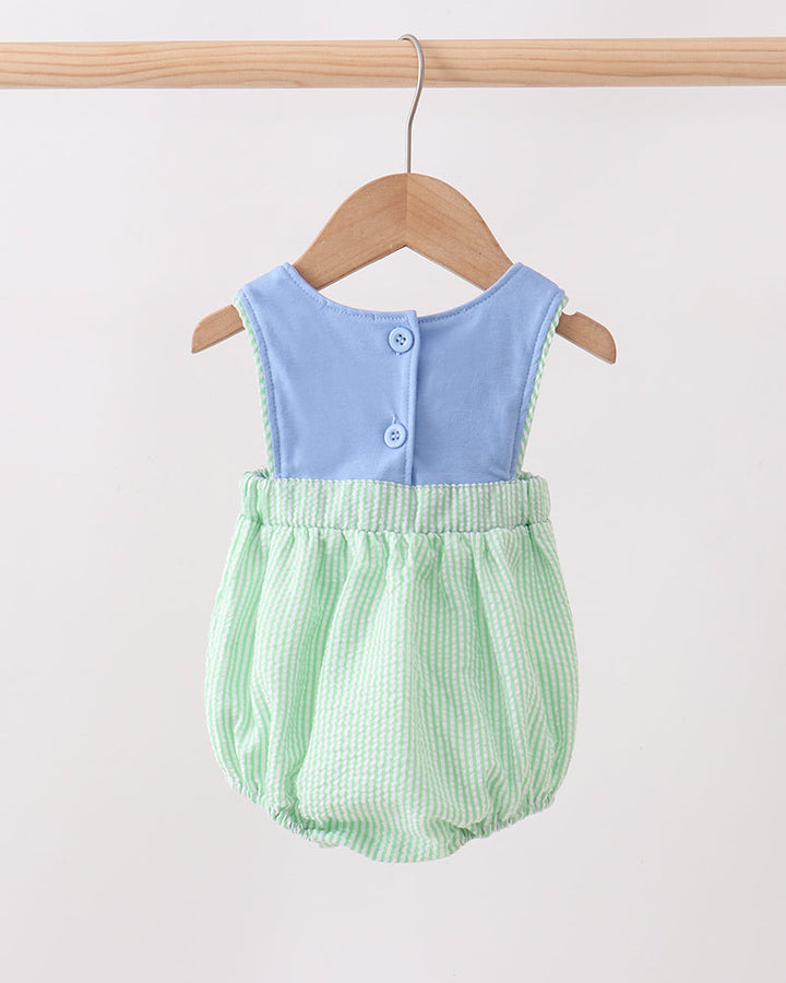 Baby romper with blue top and green checkered bottom on a wooden hanger against a white background