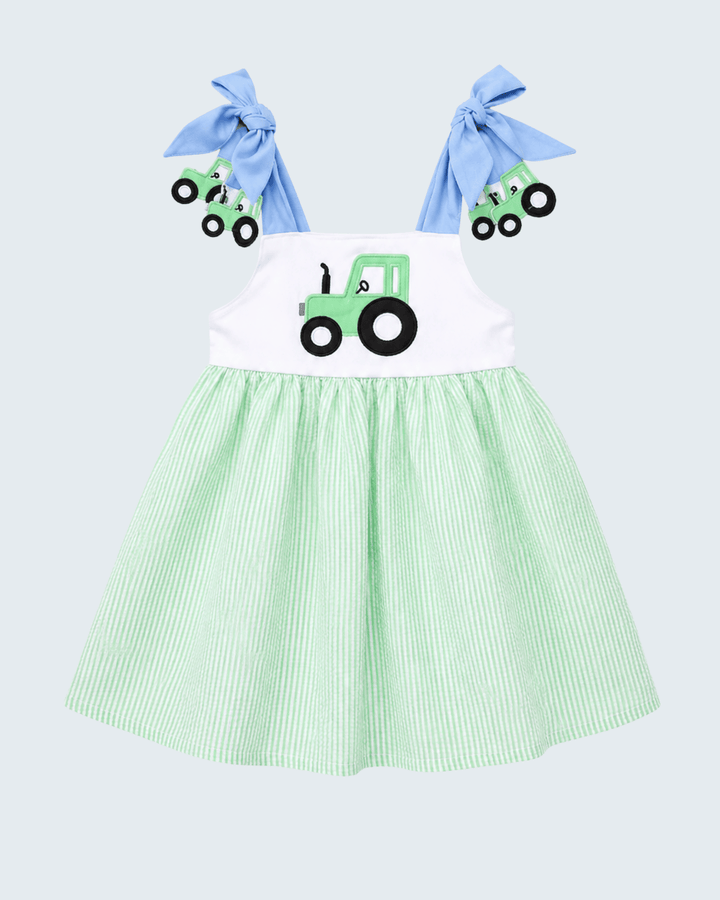Green and white dress with tractor design and blue hair bows on a light gray background
