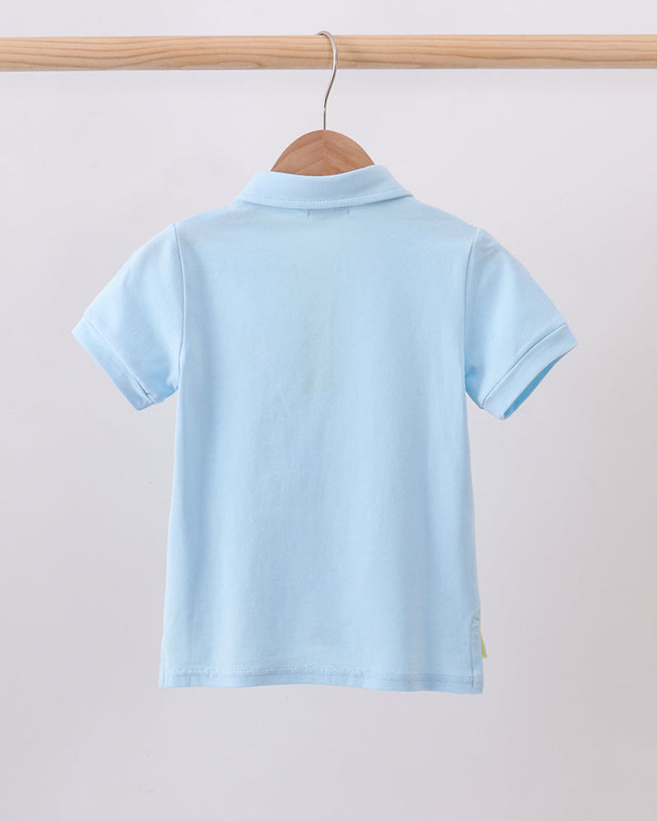A light blue short-sleeve polo shirt shown from the back, hanging on a wooden hanger from a wooden clothing rack against a plain light gray background.