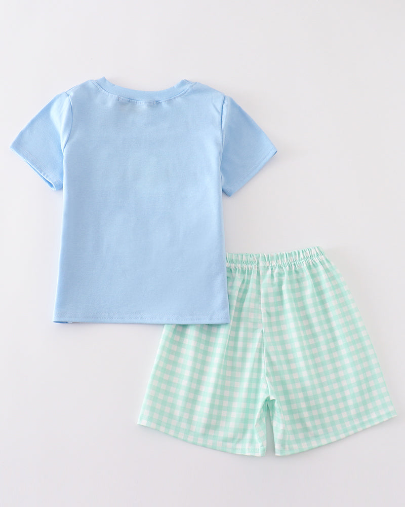 Light blue t-shirt and green checkered shorts on a light gray background
