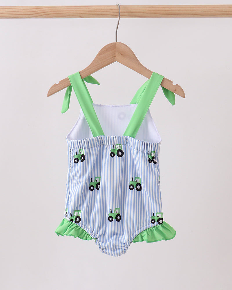 Baby romper with green straps and tractor pattern on a hanger against a white background