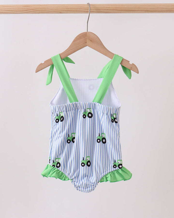 Baby romper with green straps and tractor pattern on a hanger against a white background