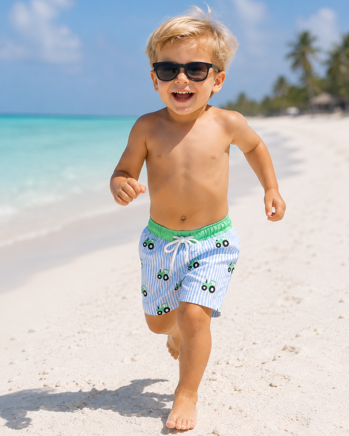 Child running on a sandy beach wearing sunglasses and swim shorts.
