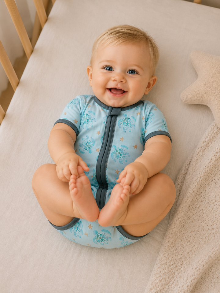 Baby sitting on a crib wearing a blue onesie with floral patterns.