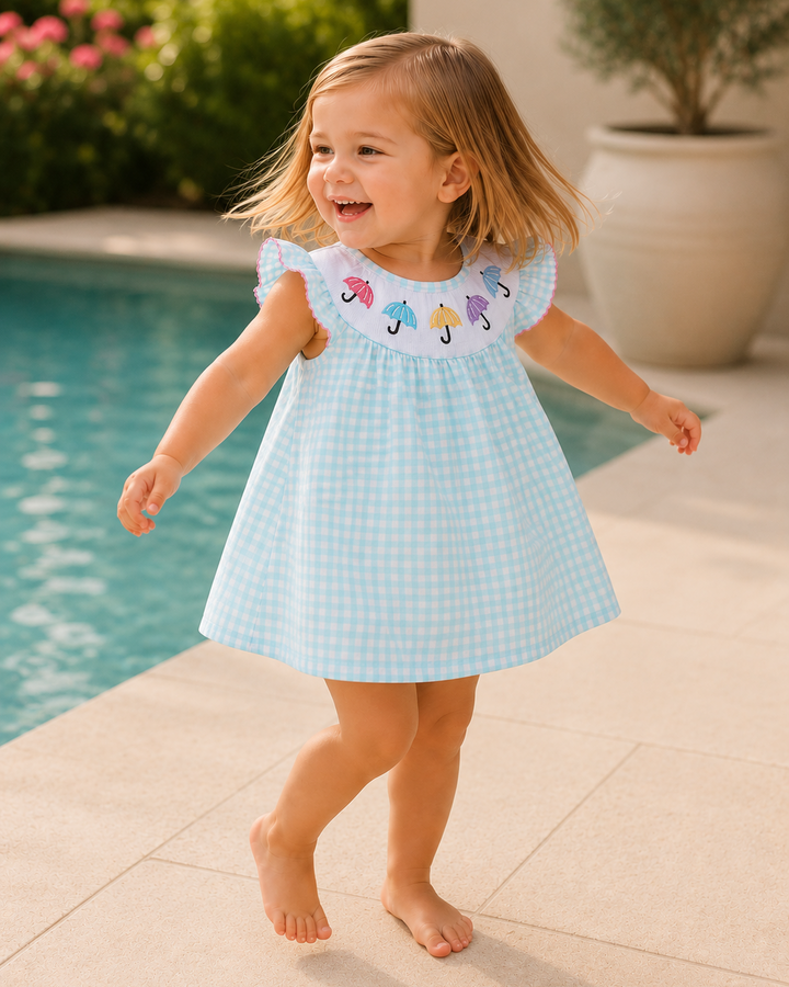 Young girl in a light blue checkered dress with umbrella pattern by a poolside.