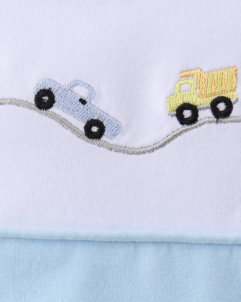 Close-up of a white and light blue garment featuring embroidered toy cars on a curved road, including a light blue car and a yellow dump truck.