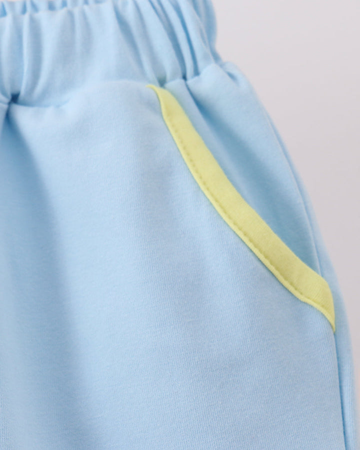 Close-up of light blue shorts with a yellow-green contrast trim detail along the side pocket, hanging on a metal hanger.