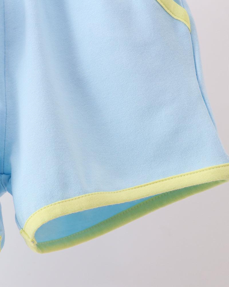 Close-up of a light blue garment, likely shorts or a skirt, with contrasting light yellow-green trim along the hem and upper side.