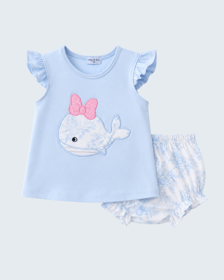 Light blue baby outfit with whale design and pink bow on a light gray background