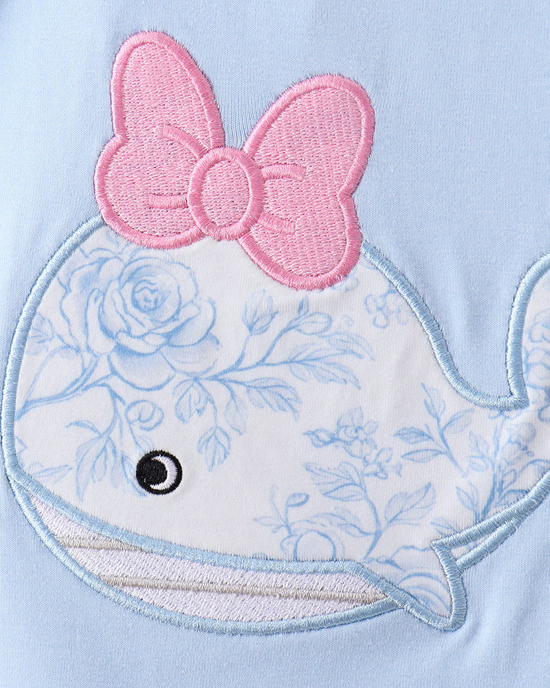 Close-up of a whale with floral design and pink bow on a light blue background