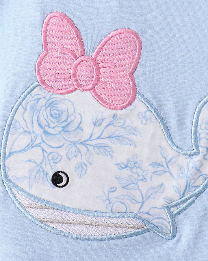 Close-up of a whale with floral design and pink bow on a light blue background