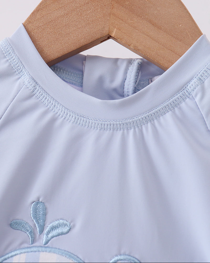 Light blue swimsuit with whale embroidery on a wooden hanger against a white background