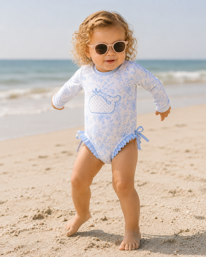 Child in a light blue swimsuit with whale design on a sandy beach.