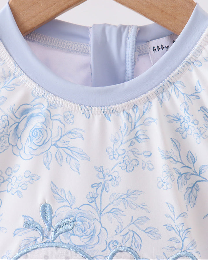 Close-up of a baby outfit with floral pattern rashguard on a hanger.