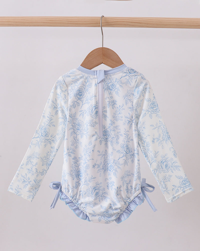 Floral-patterned baby romper on a wooden hanger against a white background