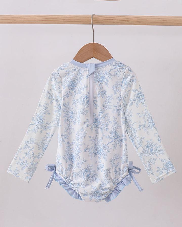 Floral-patterned baby romper on a wooden hanger against a white background