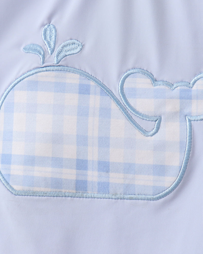 Close-up of a baby outfit with a whale design and plaid pattern on a light blue background.