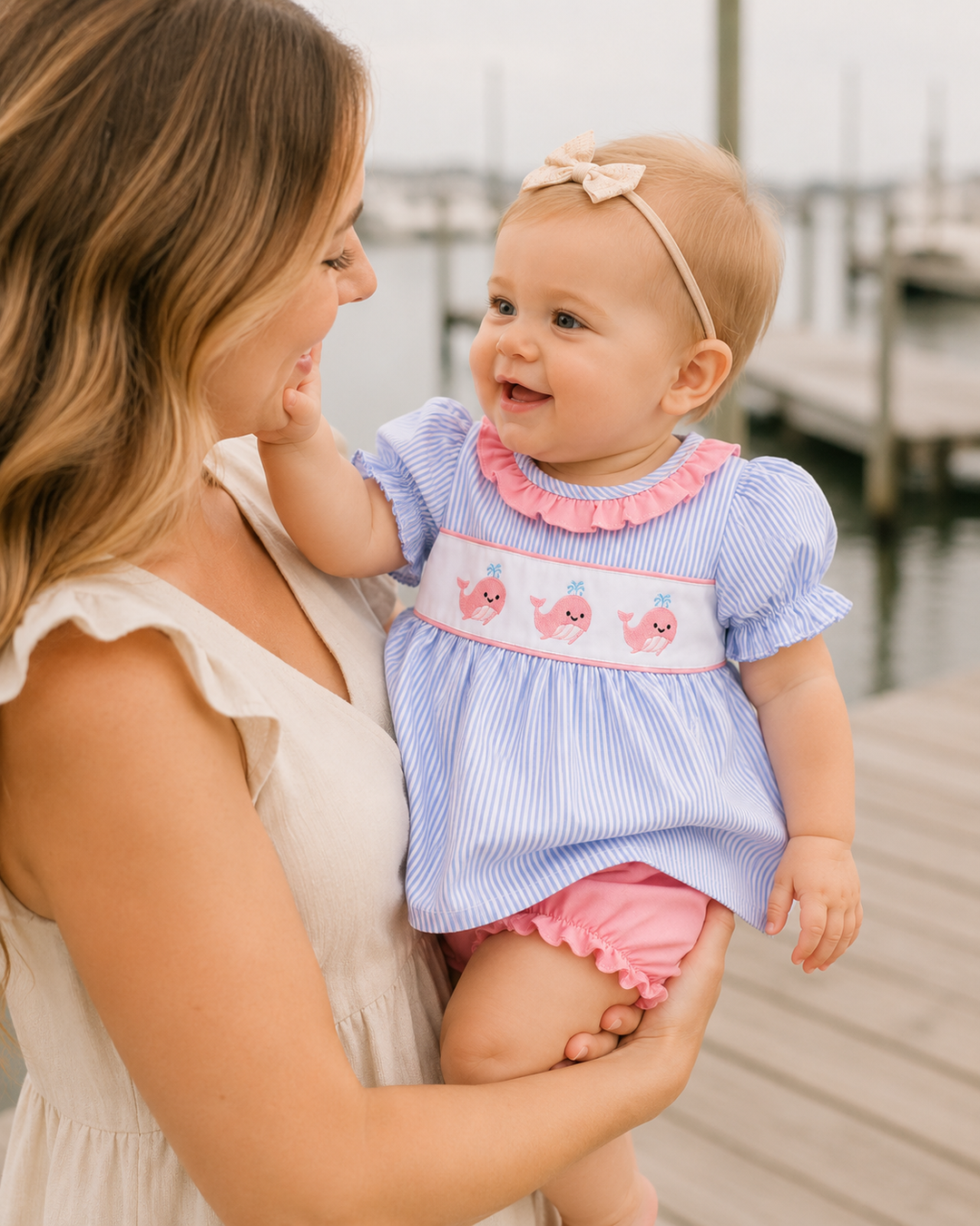 Woman holding a baby on a dock, both wearing matching outfits.
