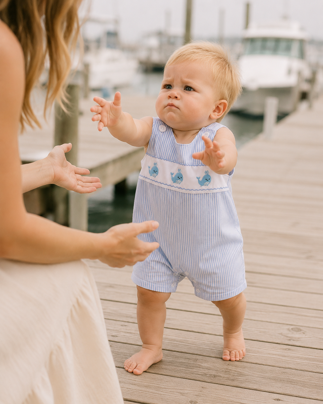 Baby in a striped romper standing on a wooden dock with a blurred background