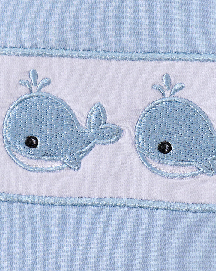 Two embroidered whale designs on a light blue fabric background