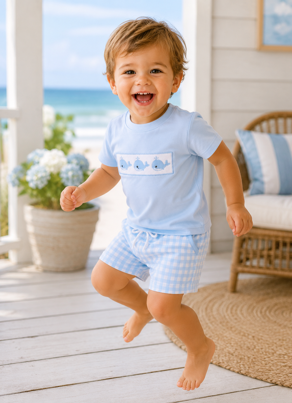 Child wearing a light blue outfit with whale design on a wooden deck with ocean view