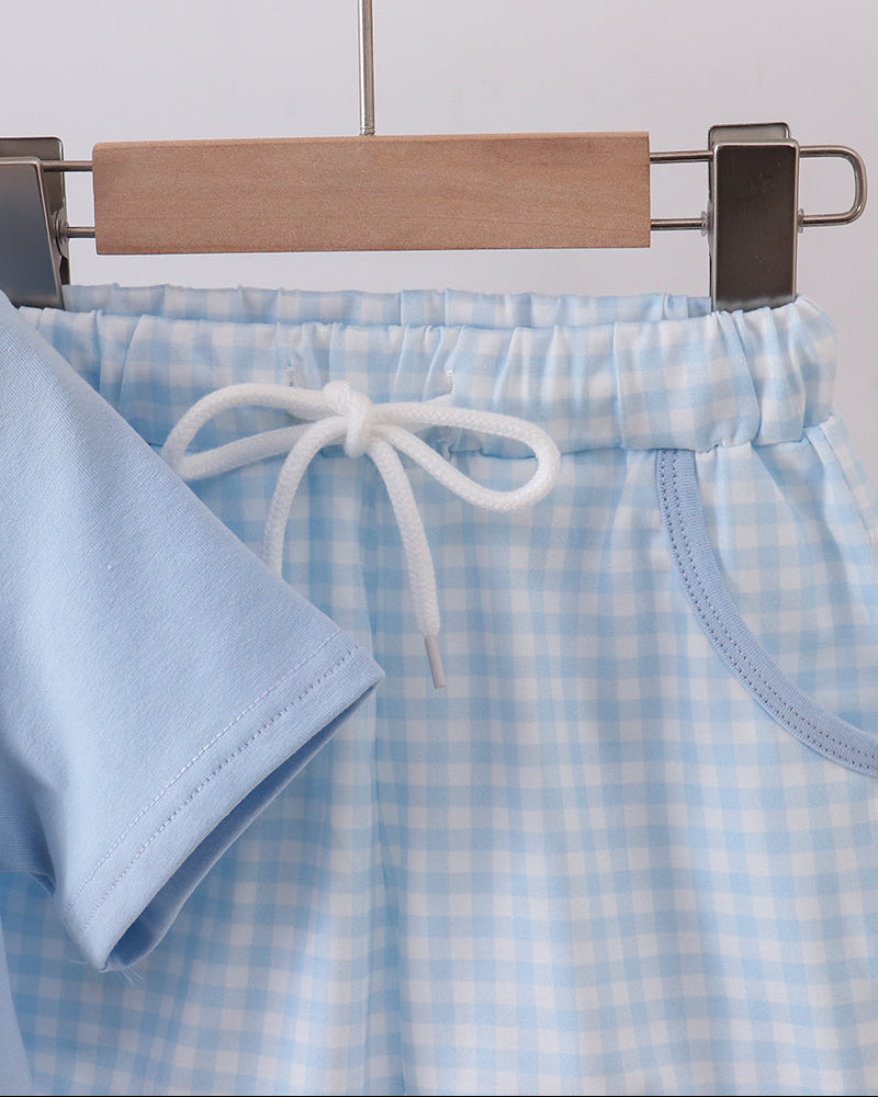 Light blue checkered shorts with a drawstring on a wooden hanger against a light gray background